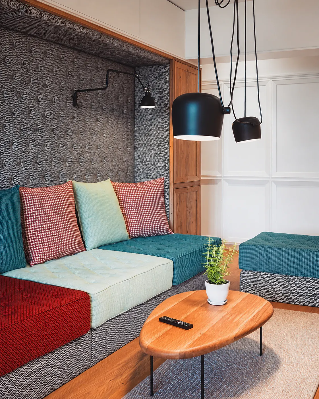 Sala de apartamento reformada com sofá planejado colorido e luminárias pendentes