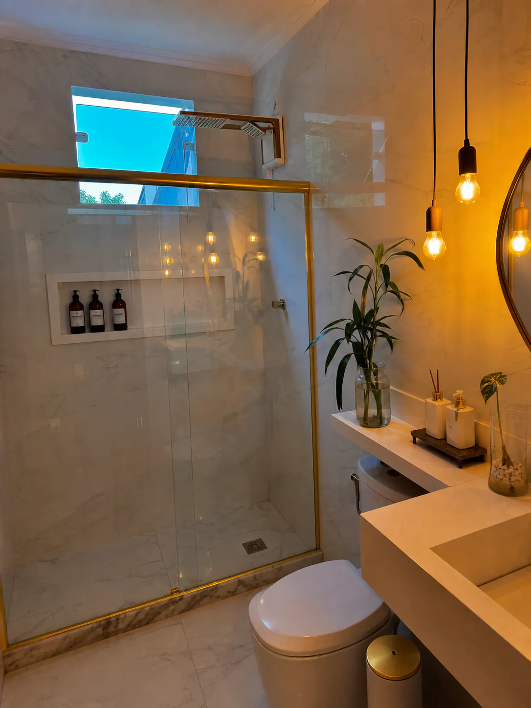 Banheiro reformado com revestimento claro, box dourado e iluminação pendente